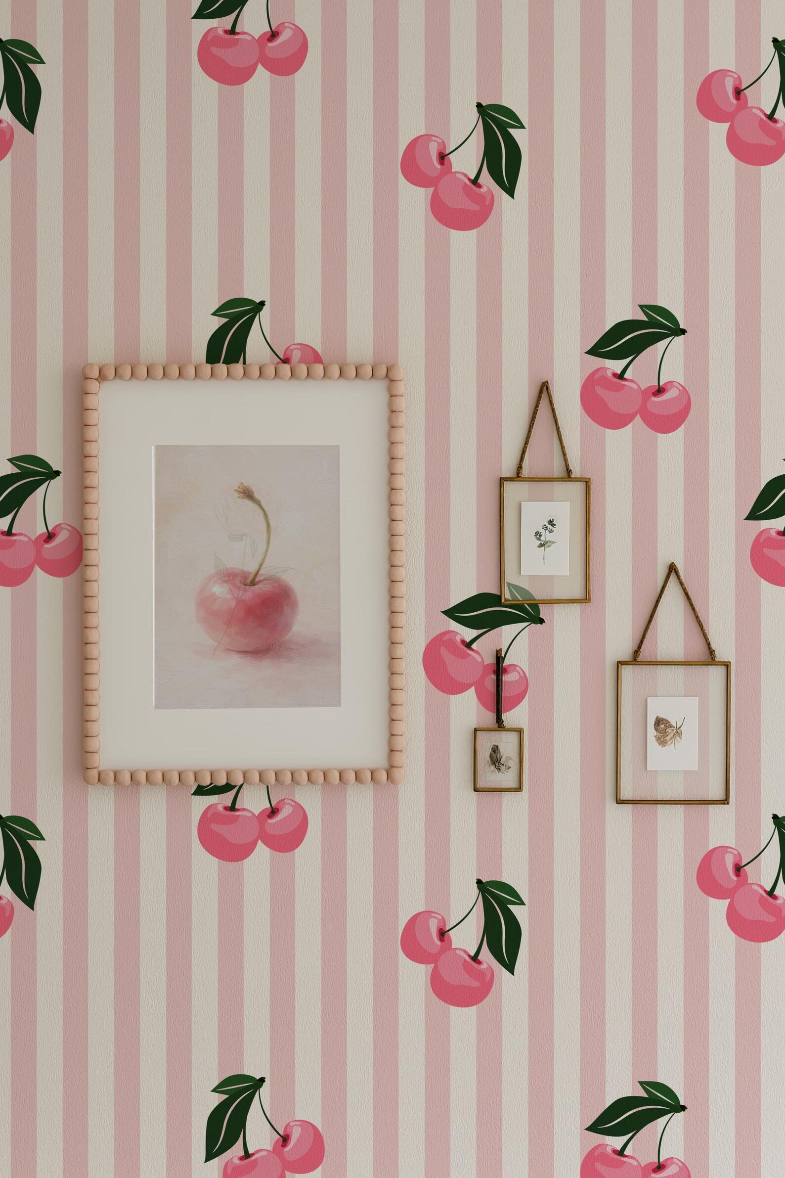 a wallpapered wall with a framed picture of a pink apple, two smaller framed pictures, and a framed picture of cherries. The wallpapered wall has a pink and white striped pattern, and the overall color scheme is predominantly pink and white.