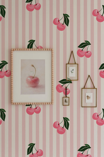 a wallpapered wall with a framed picture of a pink apple, two smaller framed pictures, and a framed picture of cherries. The wallpapered wall has a pink and white striped pattern, and the overall color scheme is predominantly pink and white.
