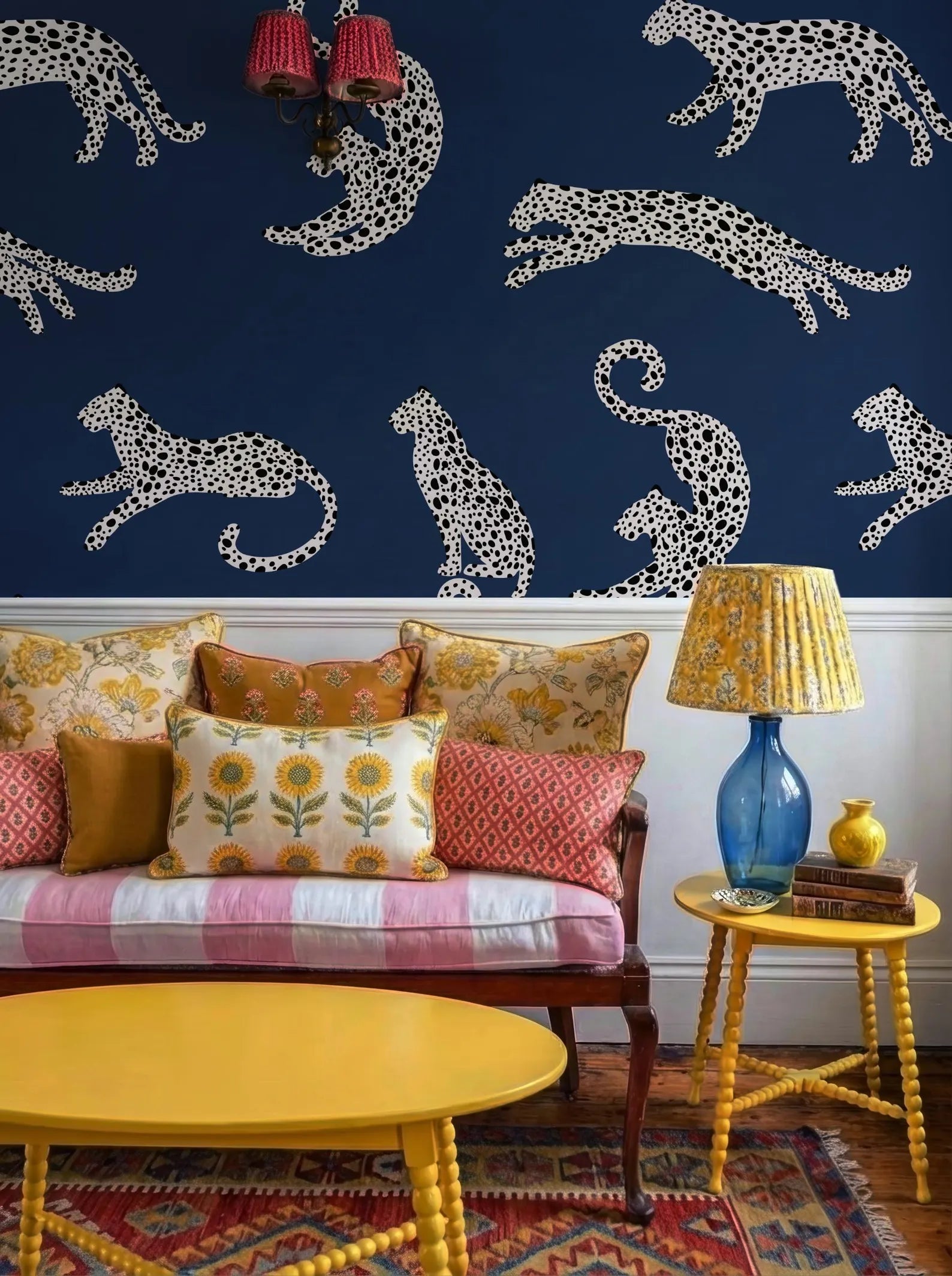 a living room with a blue wall adorned with white leopard print designs. The room is furnished with a yellow sofa, a yellow coffee table, and a yellow side table with a lamp. The overall color scheme and pattern of the room create a vibrant and lively atmosphere.