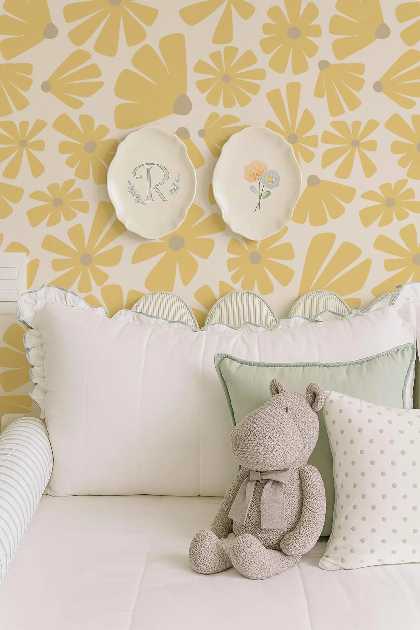 A cozy bedroom scene with a plush stuffed animal, a white bed with decorative pillows, and two plates with floral designs on the wall above the bed.