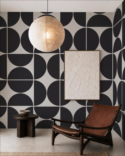 a modern living room with a black and white geometric patterned wall, a wooden chair, a round wooden table, and a large round light fixture hanging from the ceiling.