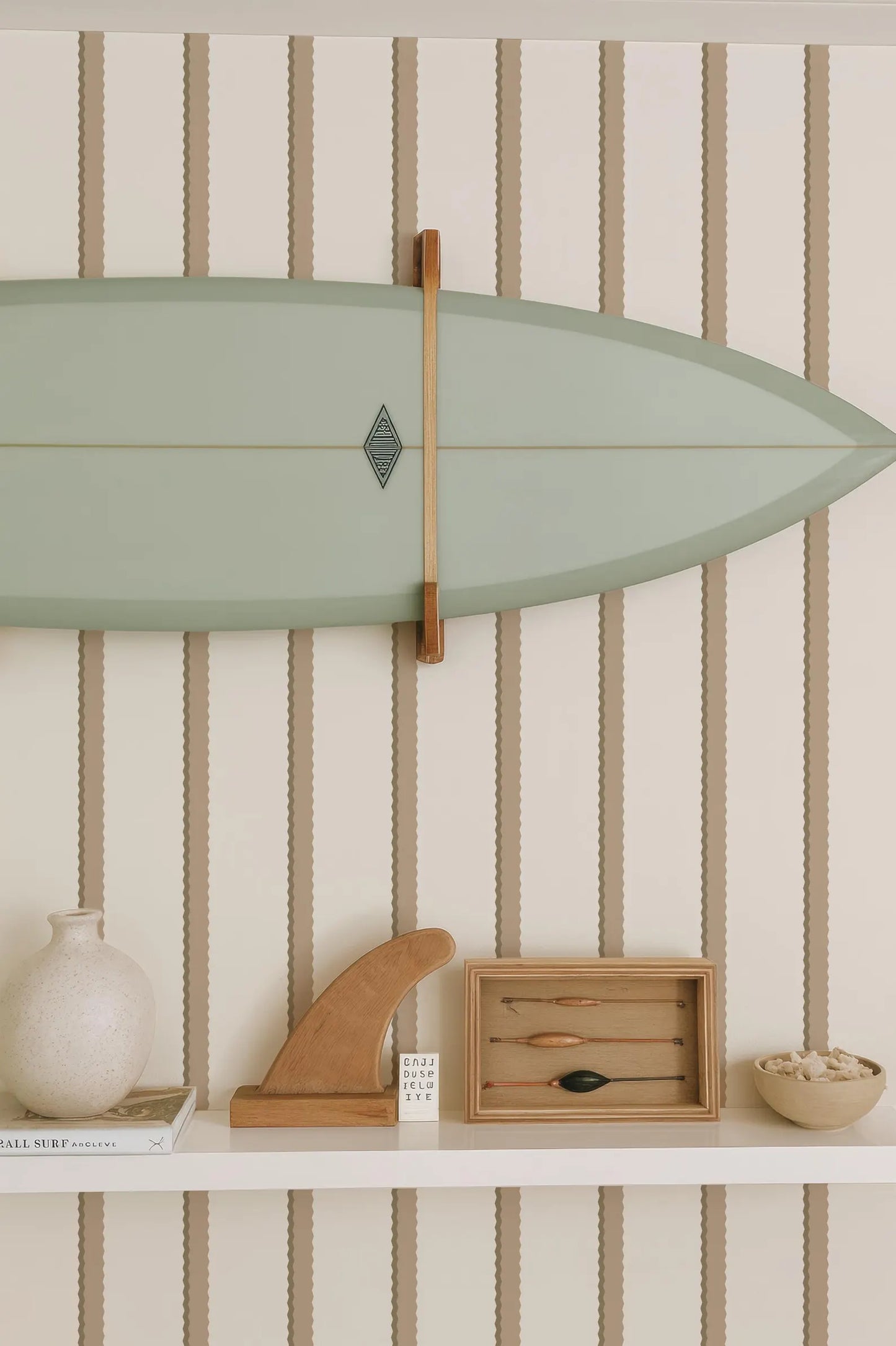 a shelf with various items, including a green surfboard, a wooden surfboard holder, a white vase, a wooden sculpture, and a small wooden box with a black object inside.