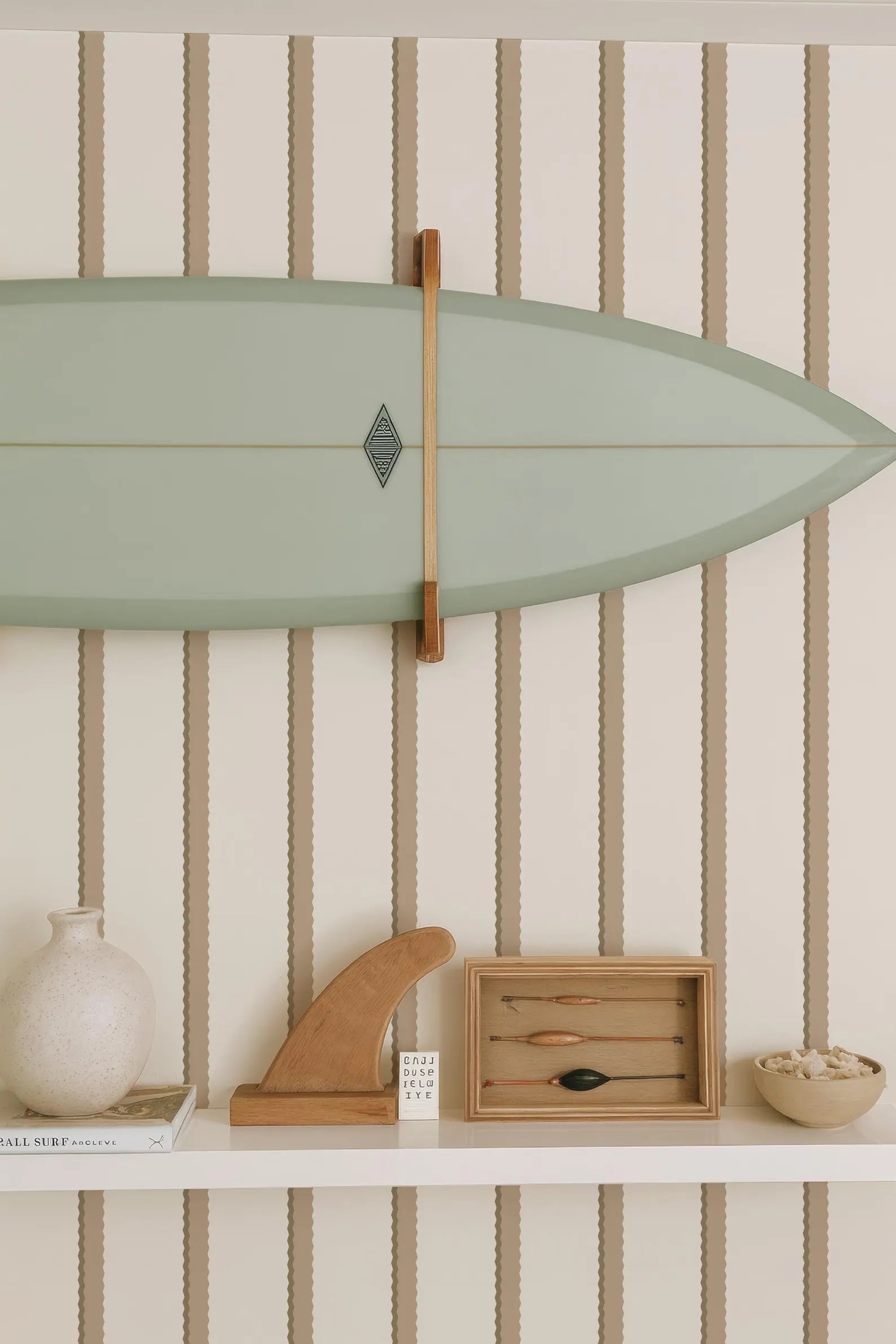a shelf with various items, including a green surfboard, a wooden surfboard holder, a white vase, a wooden sculpture, and a small wooden box with a black object inside.