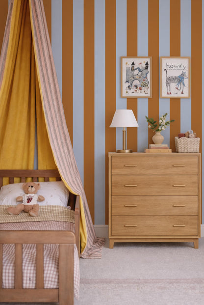 a cozy and colorful bedroom with a wooden dresser, a bed with a yellow and pink striped canopy, and framed artwork on the wall.