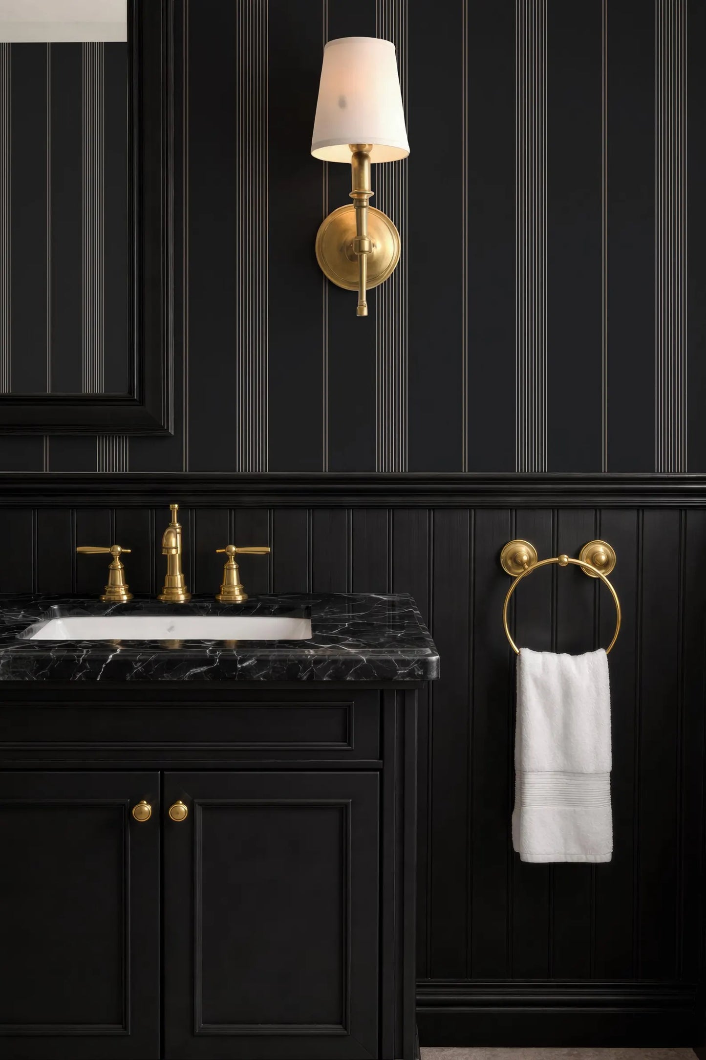 a bathroom with a black and white color scheme, including a black vanity with a marble top, a gold faucet, and a white towel hanging on a gold towel ring.