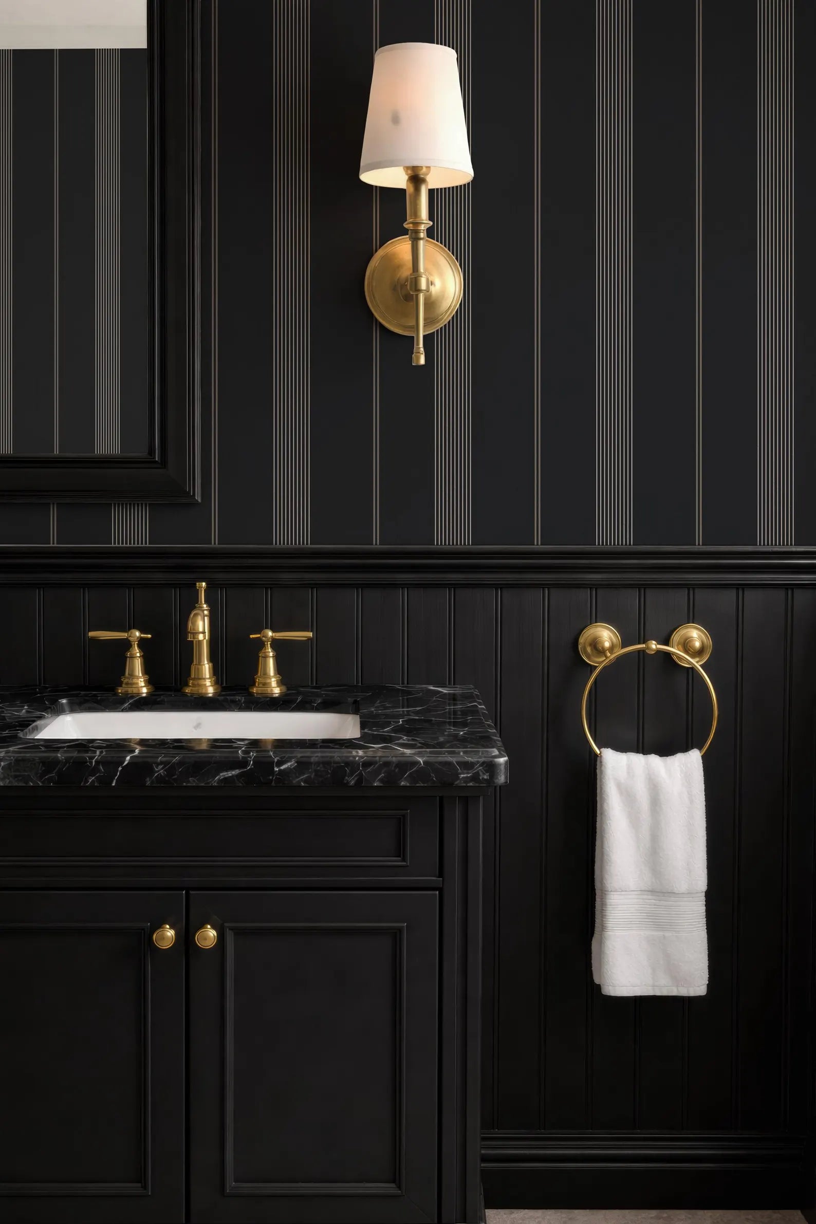 a bathroom with a black and white color scheme, including a black vanity with a marble top, a gold faucet, and a white towel hanging on a gold towel ring.