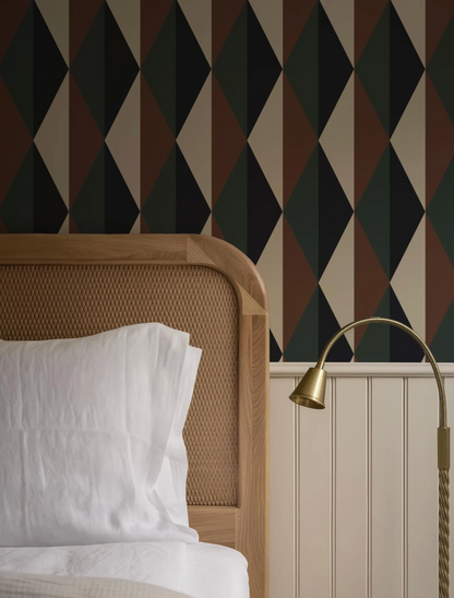 a well-made bed with a wooden headboard, a white pillow, and a gold-colored lamp on a white wall.