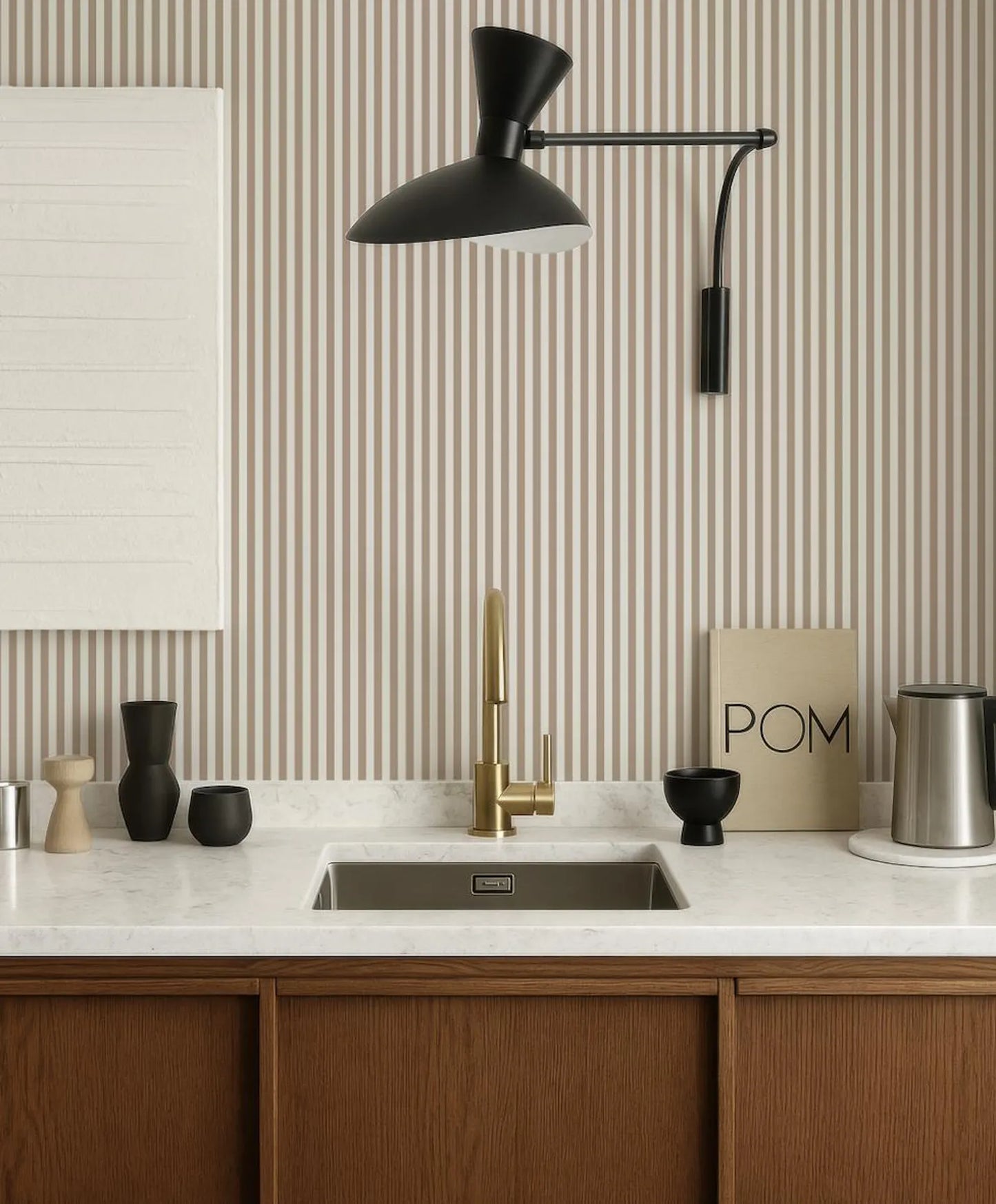 a modern kitchen with a white countertop, a gold faucet, and a black pom-pom sign. The kitchen has a striped wallpaper and a black pendant light hanging above the sink.
