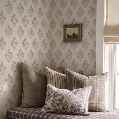 a cozy corner of a room with a plaid pillow, a striped pillow, and a floral pillow, all resting on a bed. The wall behind the pillows is covered in a patterned wallpaper, and there is a framed picture hanging on the wall.