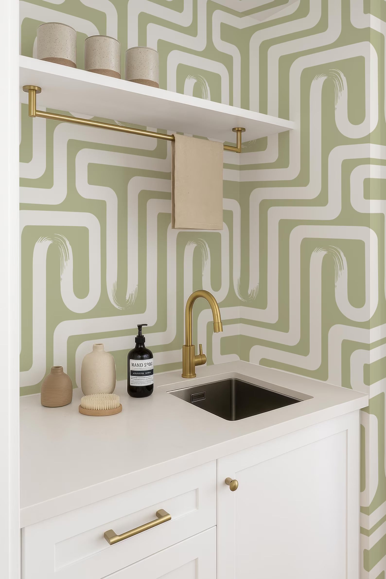 a modern bathroom with a white countertop, a gold faucet, and a shelf with decorative items. The walls are covered in a green and white patterned wallpaper, creating a visually striking contrast. The overall design is minimalist and elegant, with a focus on clean lines and a sense of simplicity.