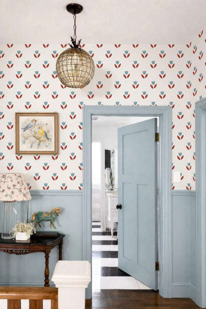 a cozy and charming entryway with a blue door, a chandelier, and a floral wallpaper. The door is open, revealing a hallway beyond. The room features a wooden table with a horse figurine, a lamp, and a painting on the wall. The overall color scheme is a harmonious blend of blue, white, and red, creating a warm and inviting atmosphere.