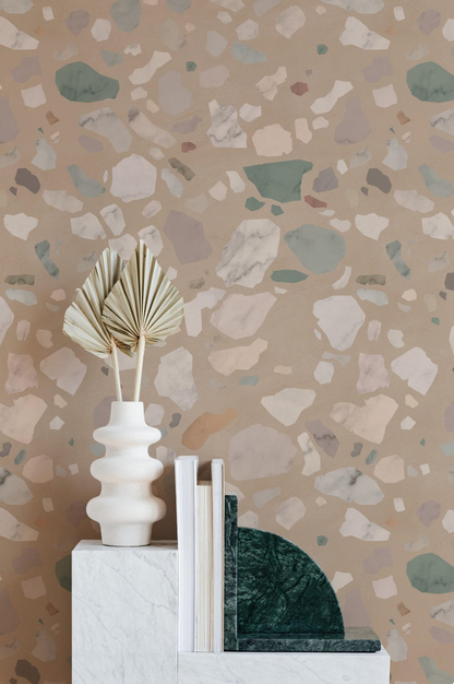 a white vase with two green leaves, a stack of books, and a green marble bookend on a white marble pedestal against a textured wall with a mosaic pattern.