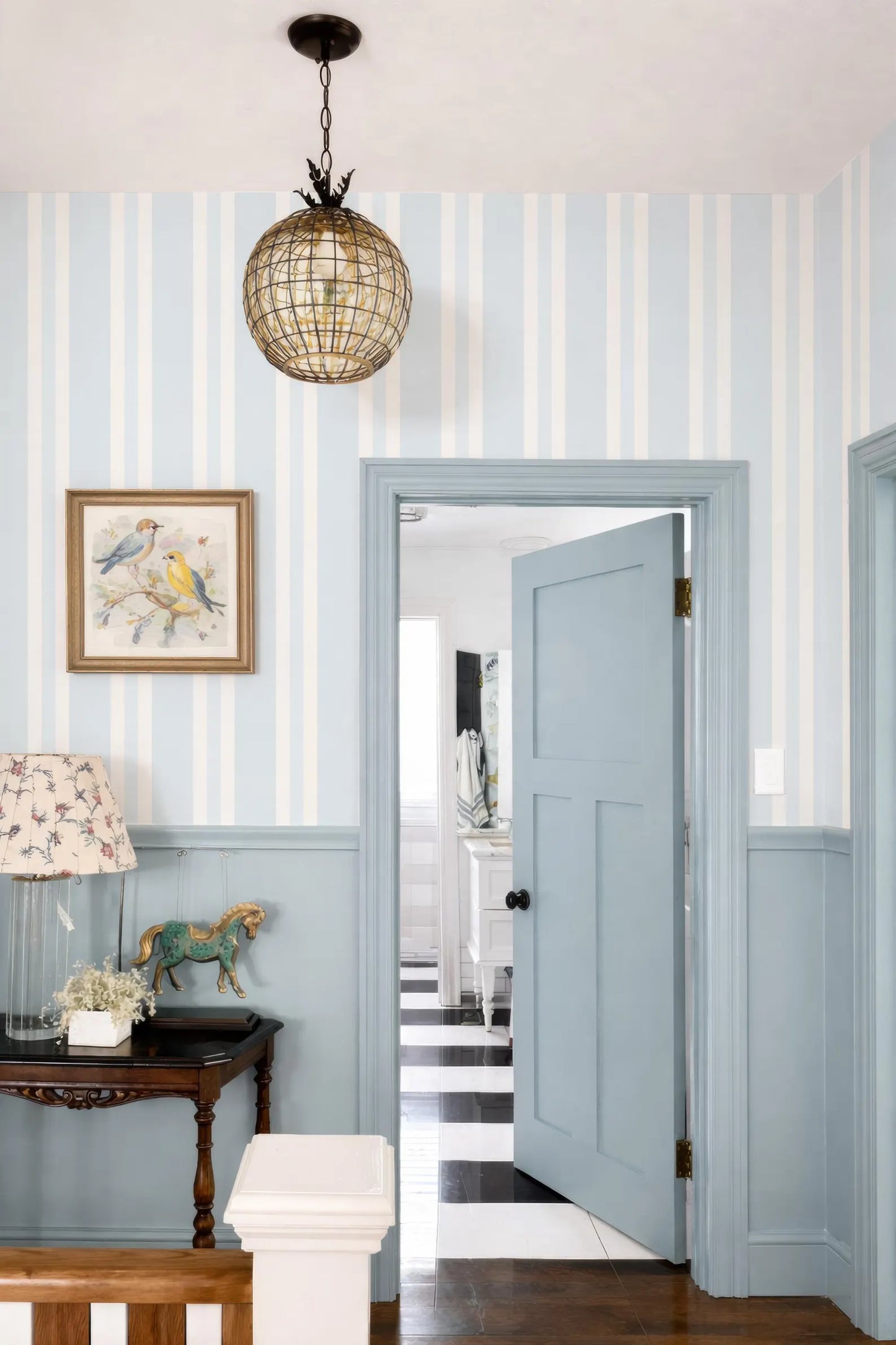 a cozy and charming interior with a blue and white striped wall, a wooden table with a horse figurine, and a chandelier hanging from the ceiling.