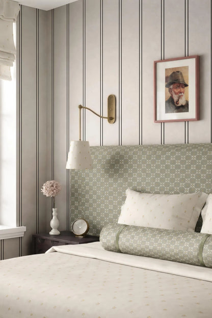 a cozy bedroom with a bed, a nightstand, and a framed picture on the wall. The bed has a green and white patterned headboard, and the room has a neutral color scheme with gray and white walls.