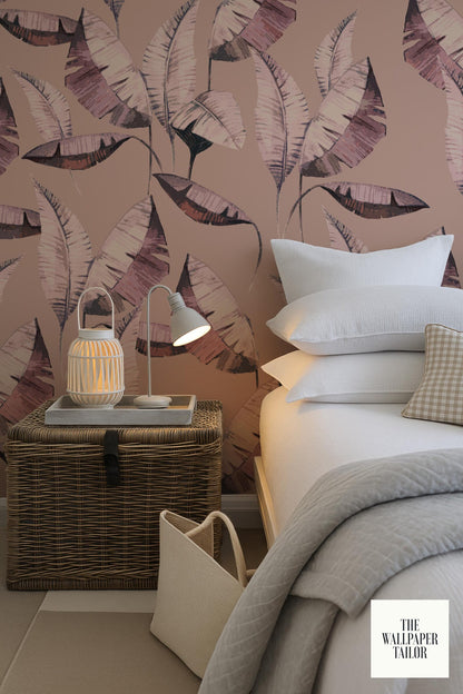 a bedroom with a bed, a nightstand, and a wicker basket. The wall behind the bed has a large, colorful, leaf-patterned wallpaper.