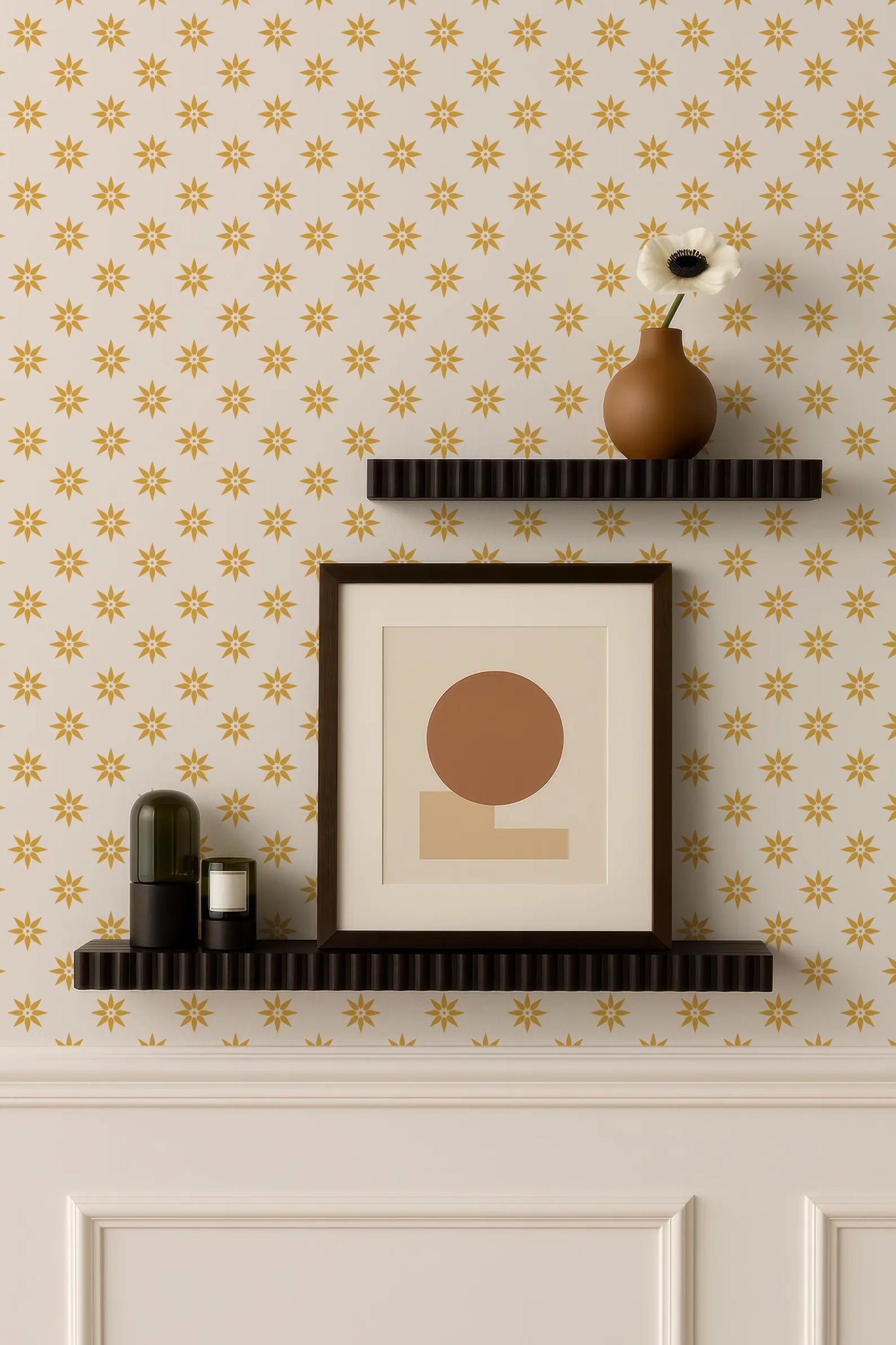 a wall with a patterned wallpaper, two black shelves mounted on the wall, and a framed picture and a vase on the top shelf.
