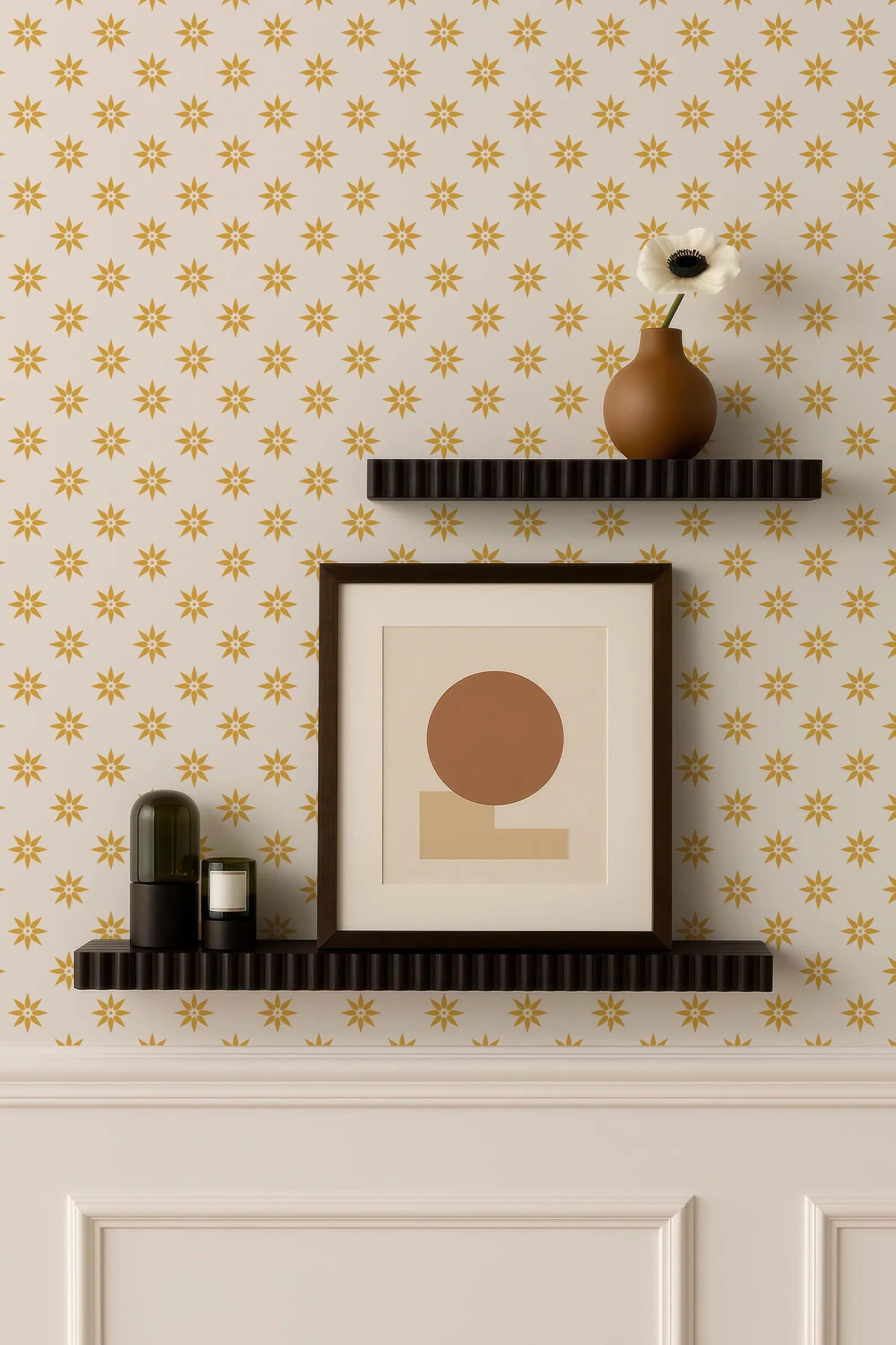 a wall with a patterned wallpaper, two black shelves mounted on the wall, and a framed picture and a vase on the top shelf.