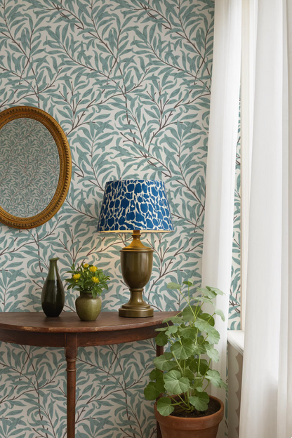a table with a lamp, a mirror, and two vases, set against a patterned wallpaper backdrop.