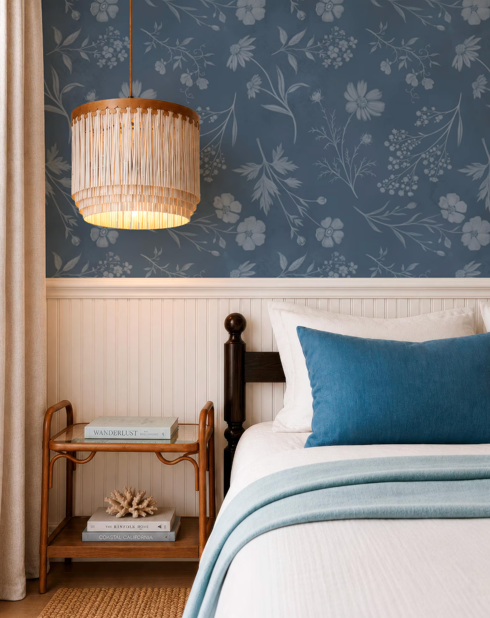 a cozy bedroom with a bed, a wooden nightstand, and a chandelier. The room has a blue floral wallpaper and a white bedspread, creating a serene and inviting atmosphere.