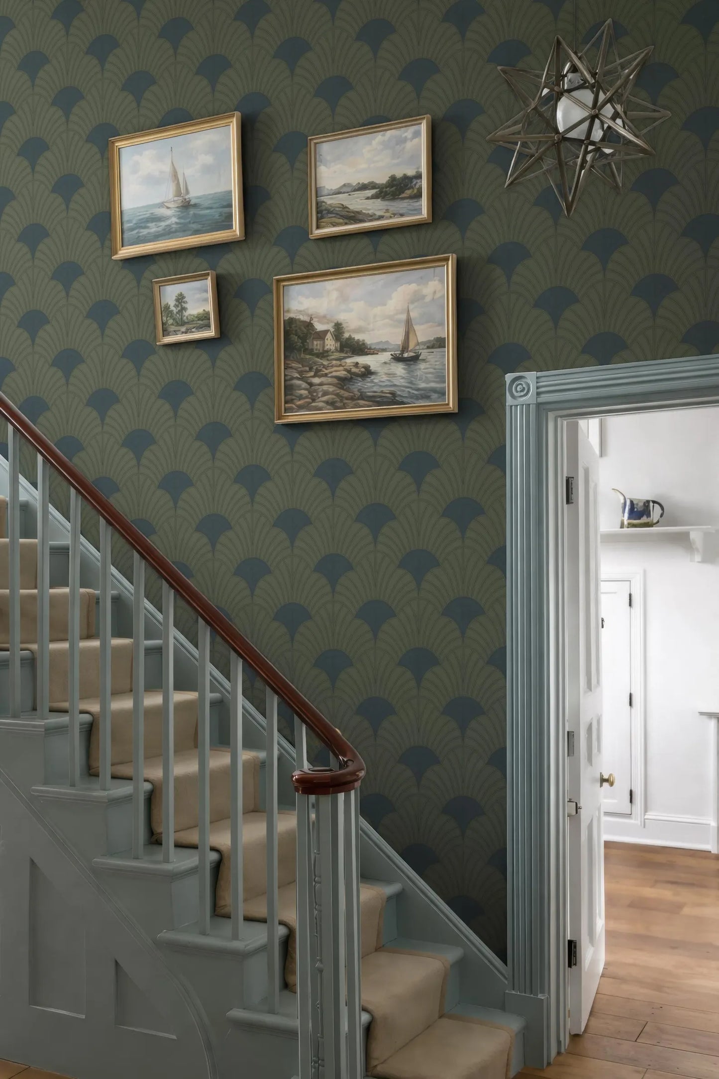a staircase with a wooden railing, a green and blue patterned wallpaper, and several framed paintings hanging on the wall above the staircase.
