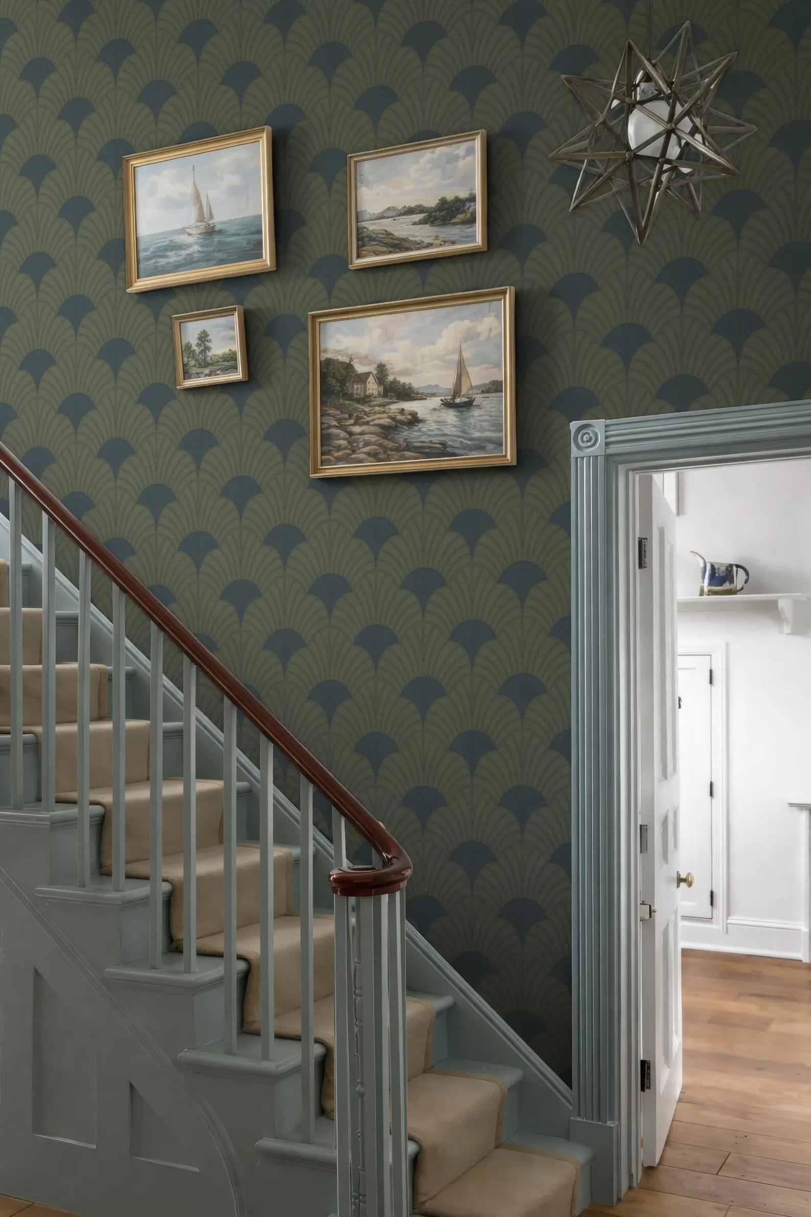 a staircase with a wooden railing, a green and blue patterned wallpaper, and several framed paintings hanging on the wall above the staircase.