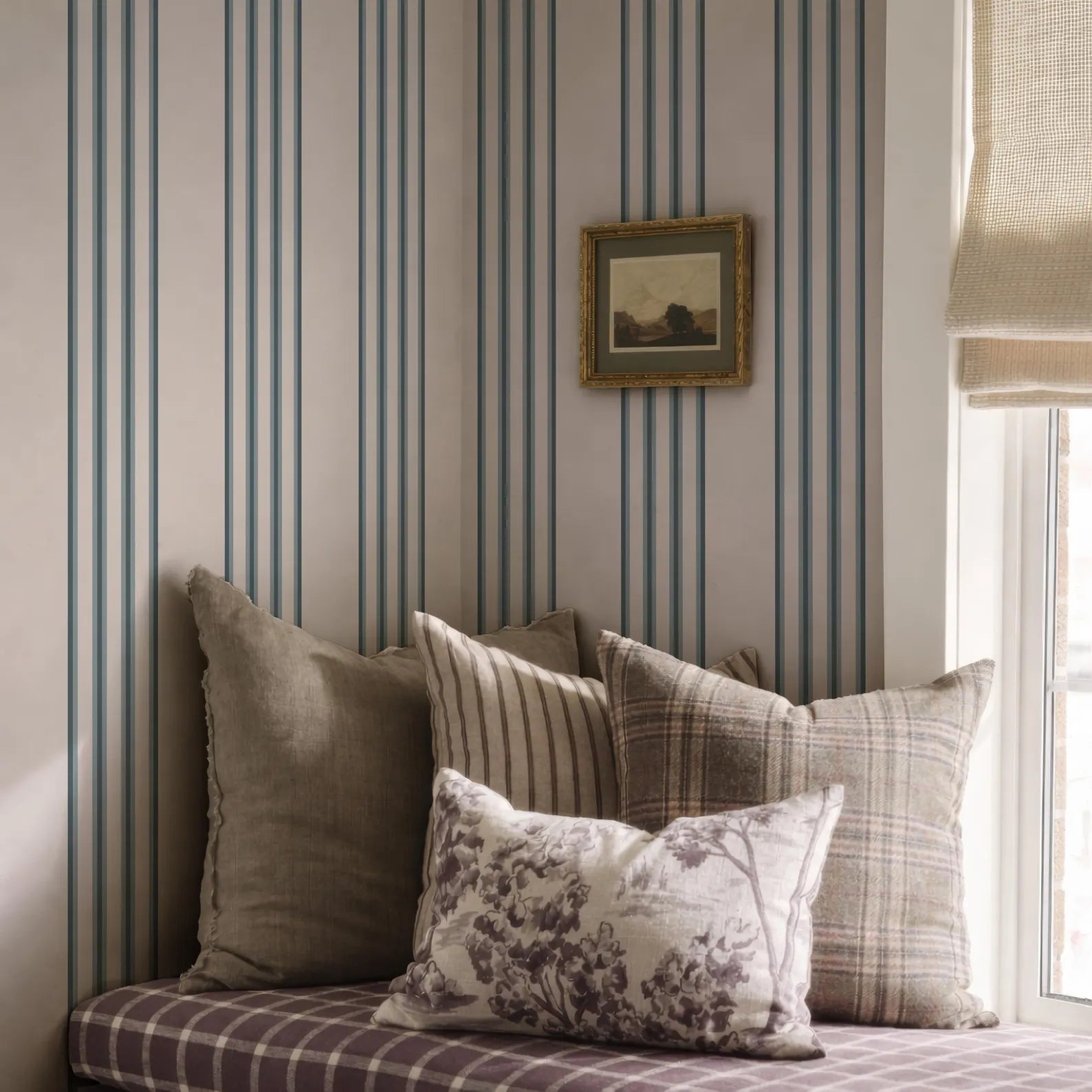 a cozy corner of a room with a plaid pillow, a striped pillow, and a framed picture on the wall.
