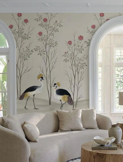 a living room with a large wall mural depicting two birds, possibly storks, standing in front of a floral background. The room has a beige sofa and a wooden coffee table, creating a cozy and inviting atmosphere.