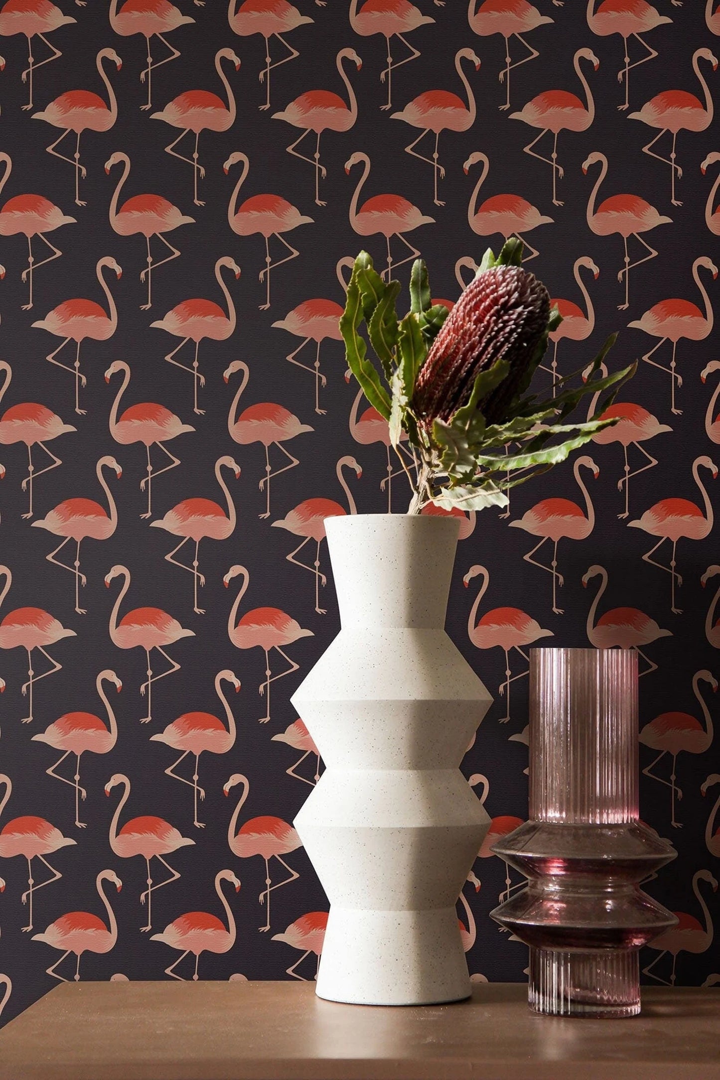 a white vase with a bouquet of flowers and a pink vase with a purple flower on a dark background with a repeating pattern of pink flamingos.