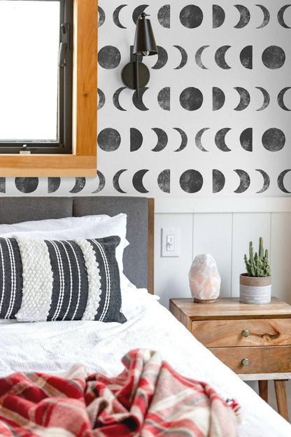 a bedroom with a bed, a nightstand, and a wallpapered wall with a repeating pattern of black and white crescent moons.