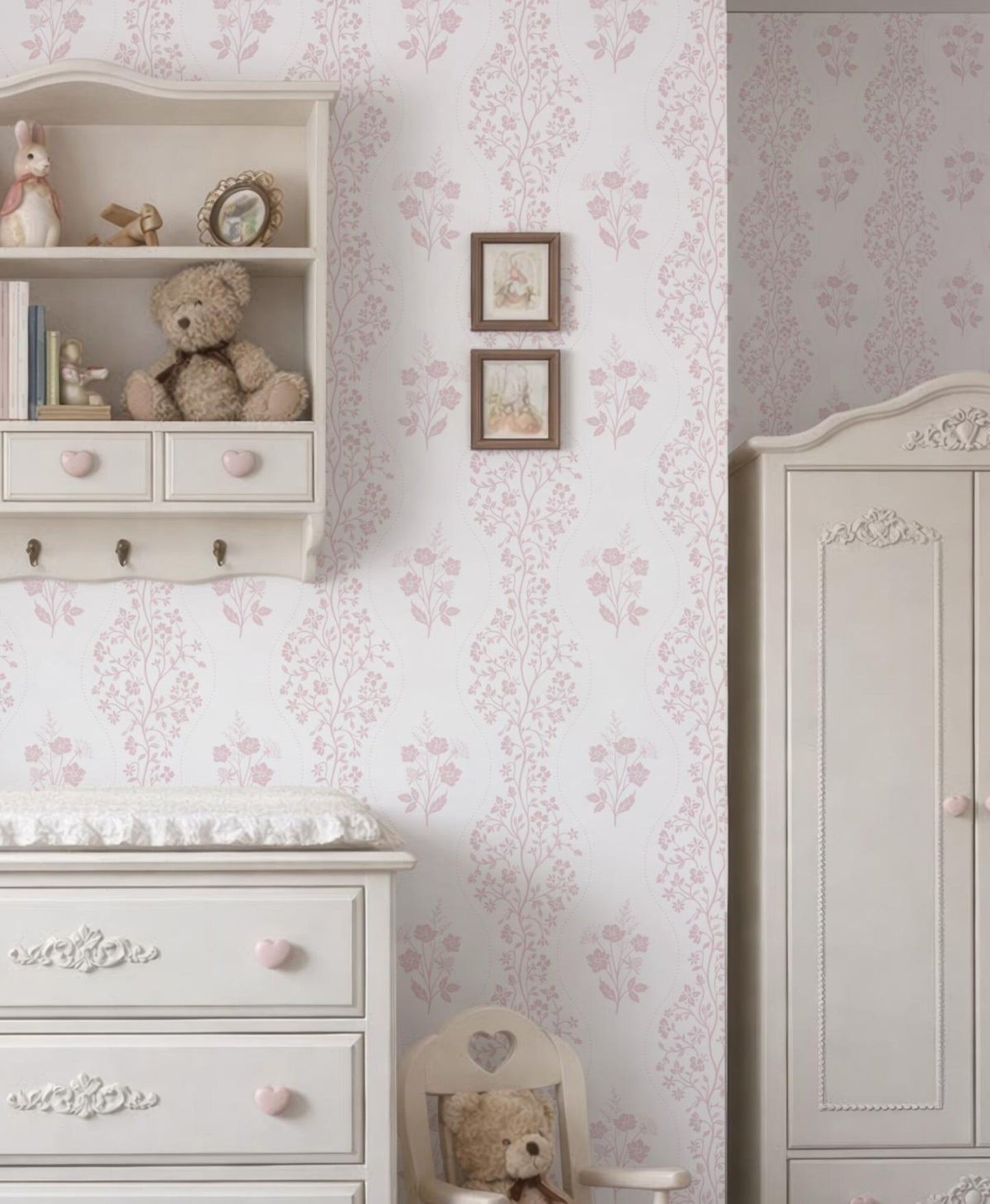 a cozy and charming nursery room with a white dresser, a shelf with stuffed animals, and a framed picture on the wall. The room has a pink and white floral wallpaper, creating a warm and inviting atmosphere.