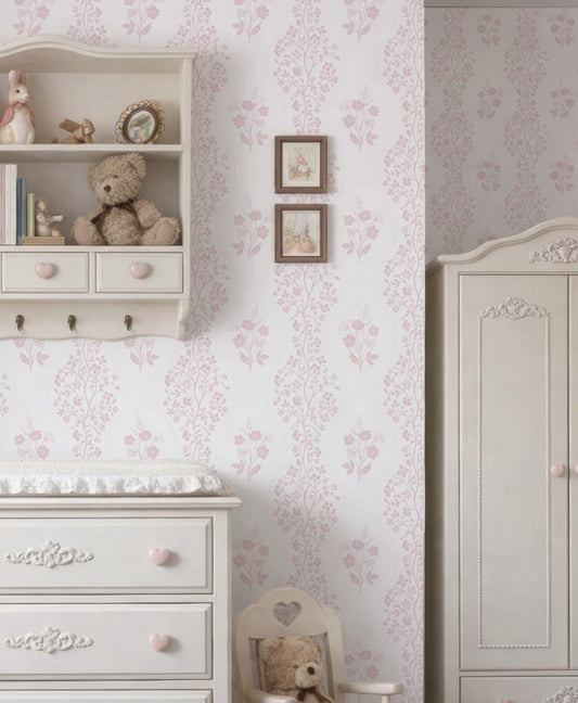 a cozy and charming nursery room with a white dresser, a shelf with stuffed animals, and a framed picture on the wall. The room has a pink and white floral wallpaper, creating a warm and inviting atmosphere.