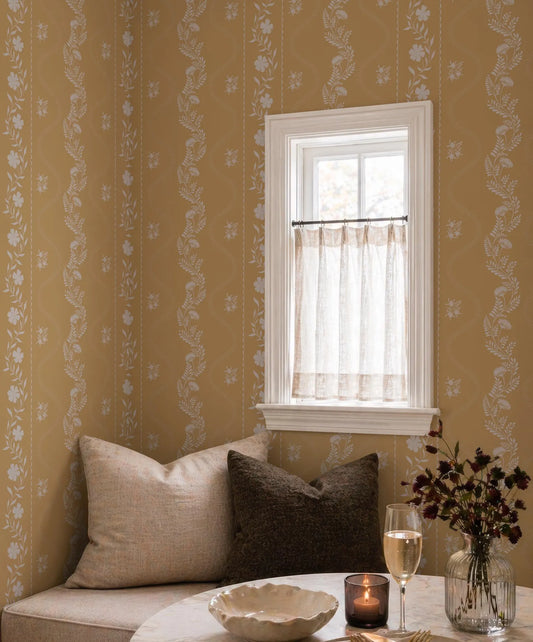 a cozy corner of a room with a window, a small table with a vase of flowers, and a bowl of fruit.
