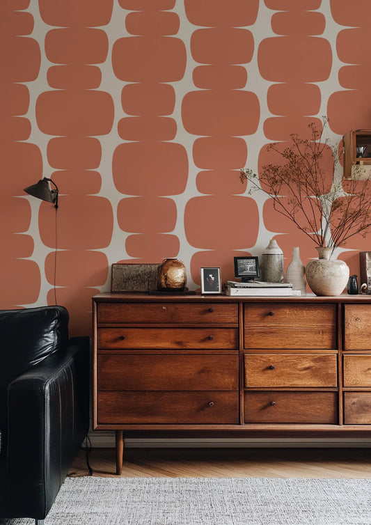 a modern living room with a wooden dresser, a black leather couch, and a patterned orange wall.