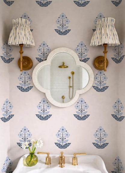 a bathroom with a white sink, a mirror, and two wall sconces with striped fabric shades. The walls are decorated with a floral pattern in shades of blue and white. There is also a vase with white flowers on the sink, adding a touch of elegance to the space.