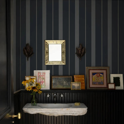 a bathroom with a black and white striped wall, a white sink, and a shelf with framed pictures and a vase of yellow flowers.