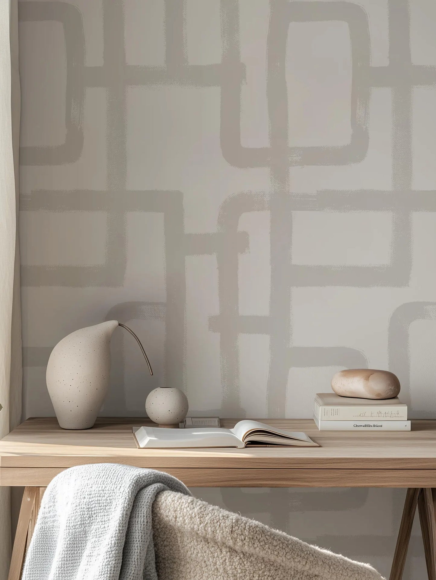 a wooden desk with a white vase, a book, and a small sculpture on it. The desk is situated in front of a wall with a geometric pattern.
