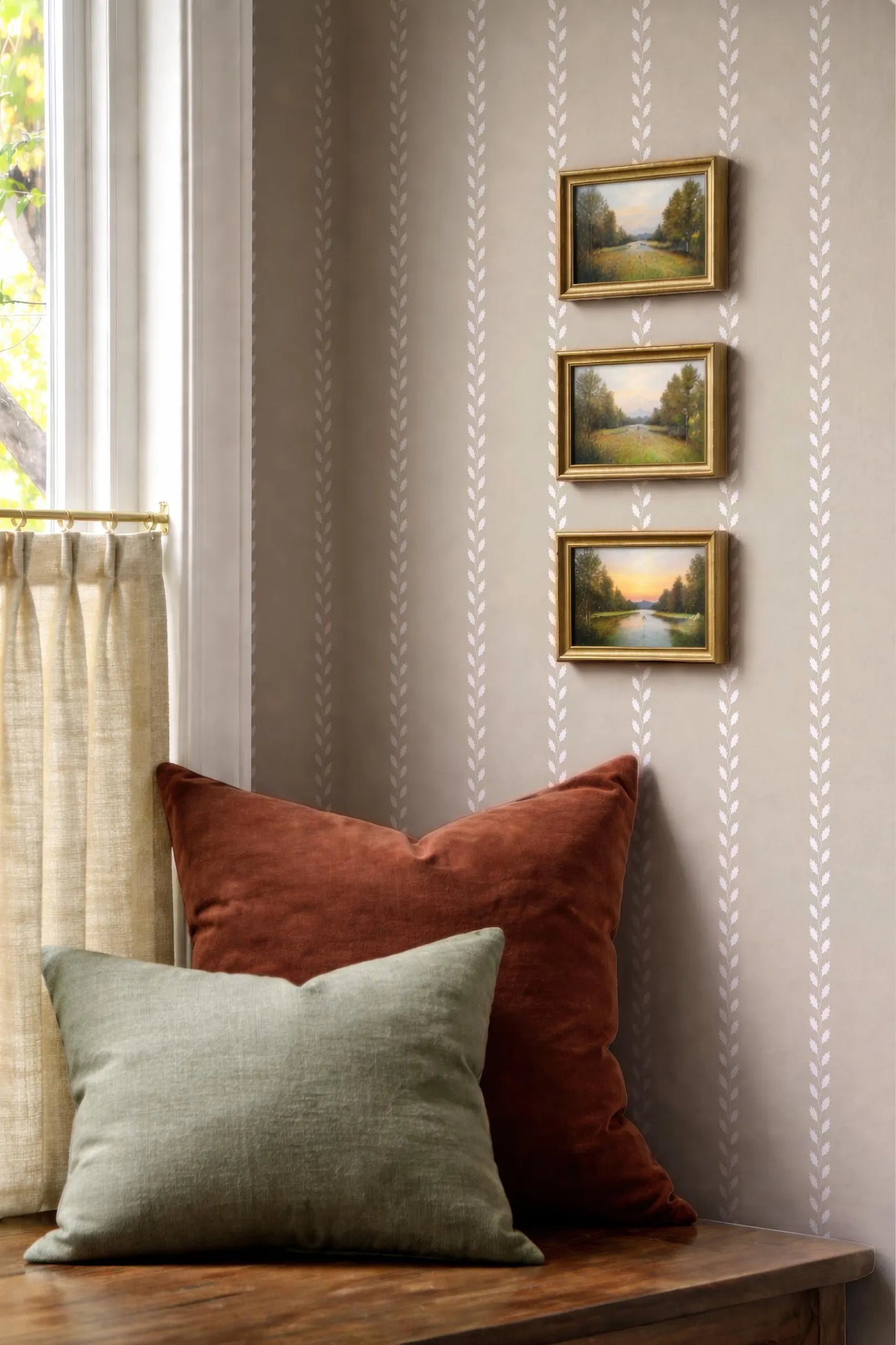 a cozy corner with a wooden table, a window with a curtain, and three framed landscape paintings hanging on the wall.