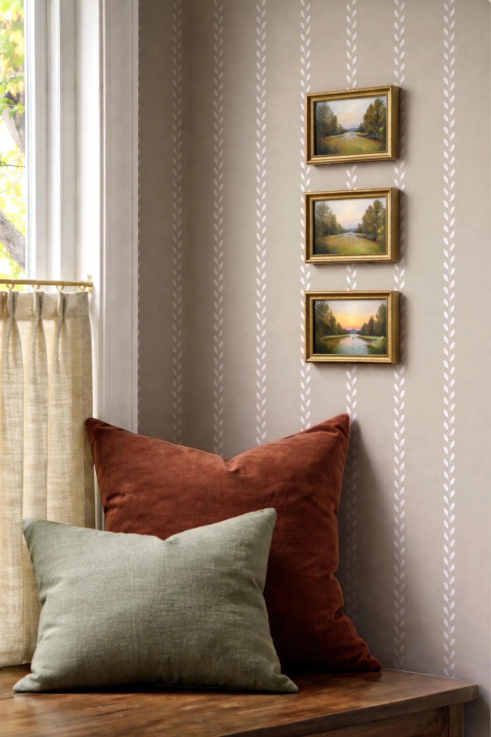 a cozy corner with a wooden table, a window with a curtain, and three framed landscape paintings hanging on the wall.