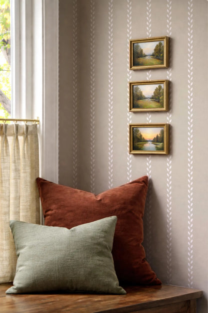 a cozy corner with a wooden table, a window with a curtain, and three framed landscape paintings hanging on the wall.