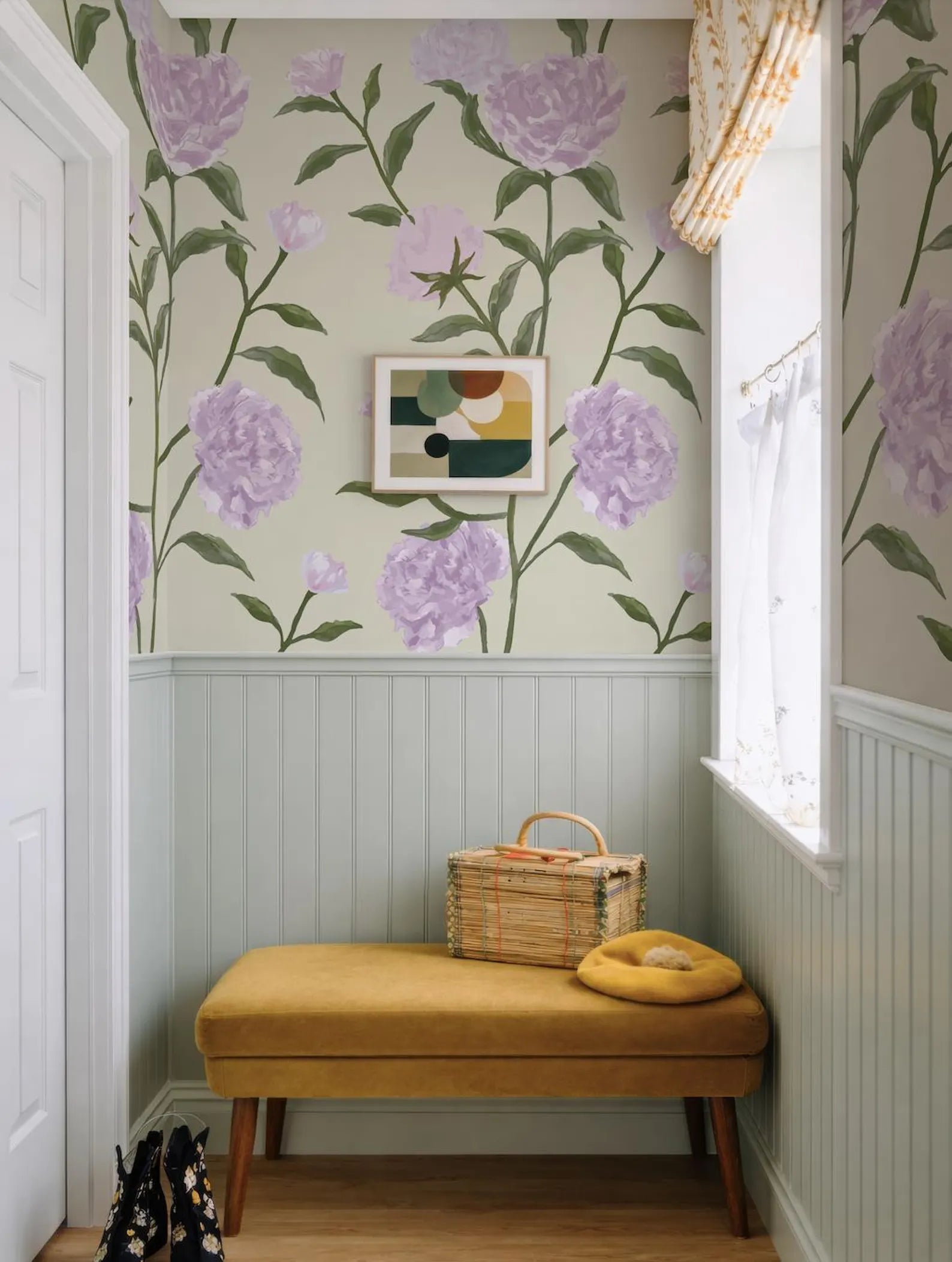 a cozy and charming hallway with a floral wallpaper pattern in shades of purple and green. A yellow bench is situated in the corner, and a woven basket rests on it. A framed abstract artwork hangs on the wall above the bench, adding a touch of artistic flair to the space.