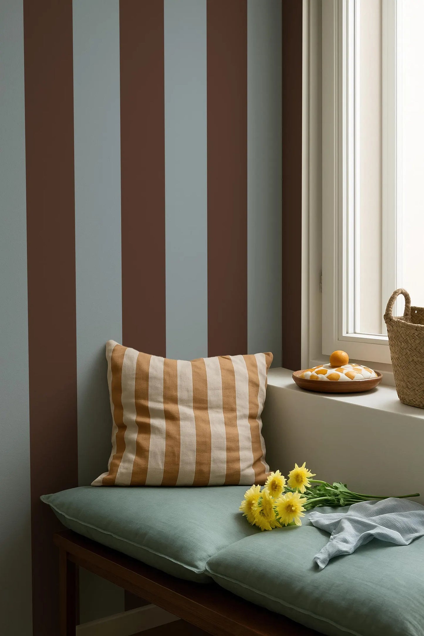 a cozy corner with a striped wall, a green bench, a striped pillow, and a basket of fruit on a windowsill.