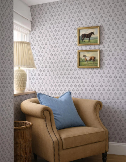 a cozy corner of a room with a beige armchair, a wicker basket, and a lamp. Above the armchair, there are two framed pictures of horses, adding a touch of nature and elegance to the space. The wall behind the armchair is adorned with a patterned wallpaper, complementing the overall design of the room.