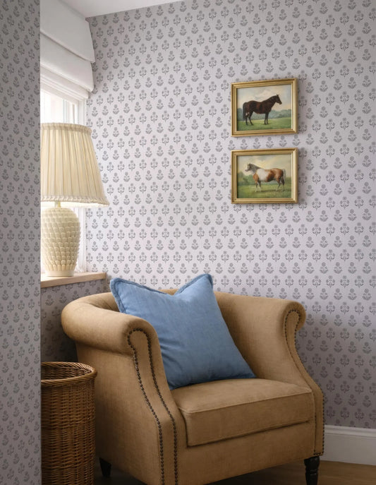 a cozy corner of a room with a beige armchair, a wicker basket, and a lamp. Above the armchair, there are two framed pictures of horses, adding a touch of nature and elegance to the space. The wall behind the armchair is adorned with a patterned wallpaper, complementing the overall design of the room.