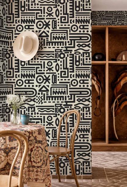 a room with a black and white patterned wall, a table with a floral tablecloth, and a wooden shelf with various items.