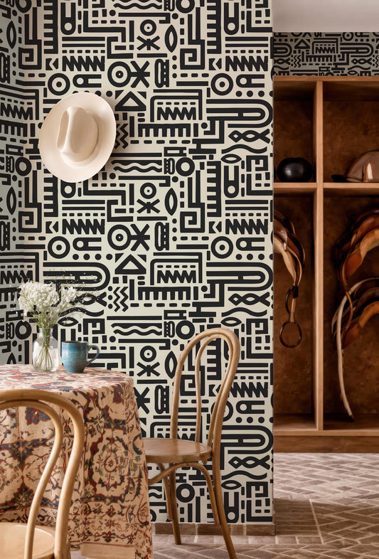 a room with a black and white patterned wall, a table with a floral tablecloth, and a wooden shelf with various items.