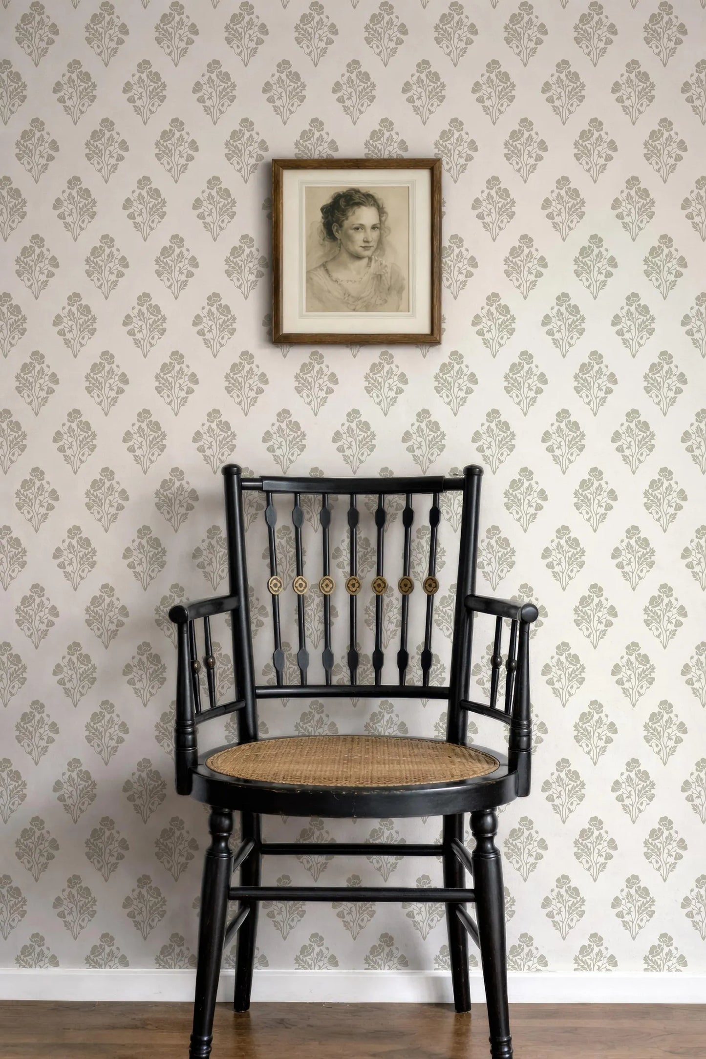a black wooden chair with a woven seat, positioned against a wall with a floral wallpaper. Above the chair, there is a framed portrait of a woman.