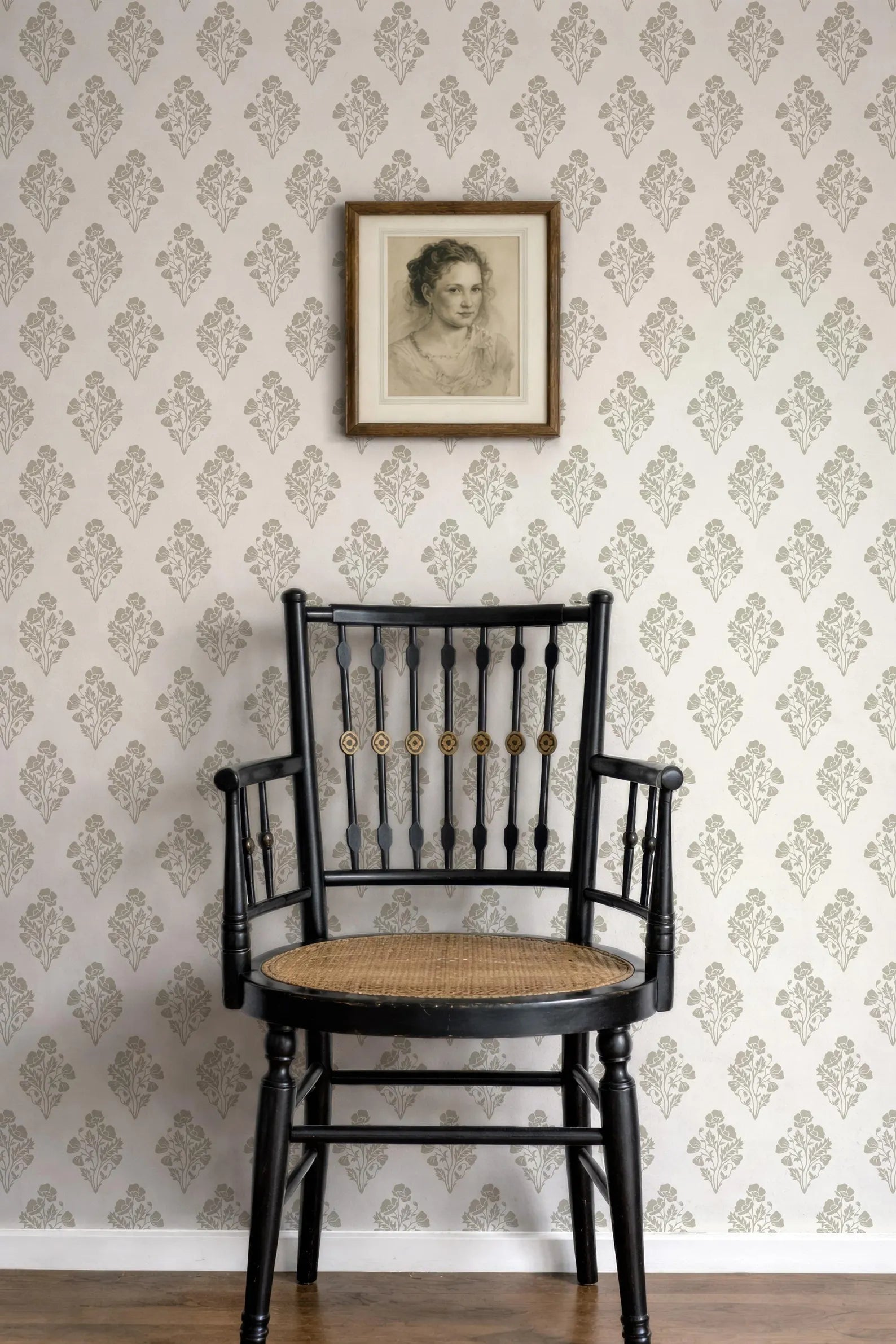 a black wooden chair with a woven seat, positioned against a wall with a floral wallpaper. Above the chair, there is a framed portrait of a woman.