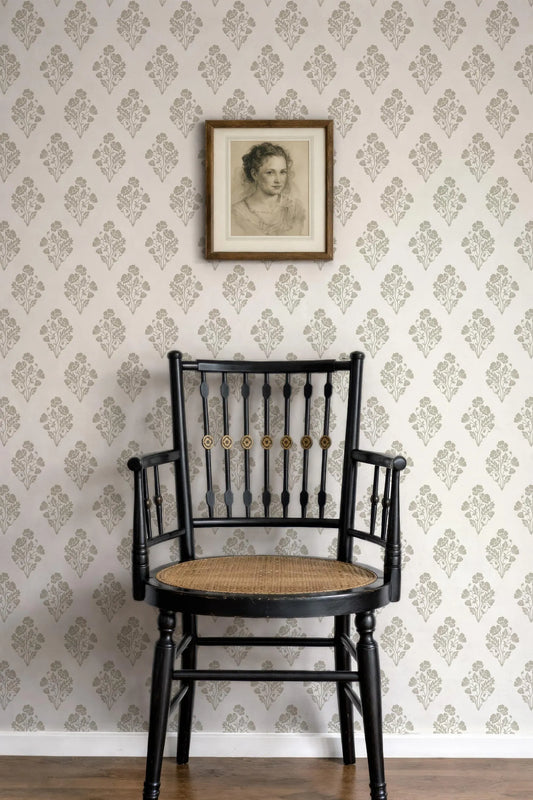 a black wooden chair with a woven seat, positioned against a wall with a floral wallpaper. Above the chair, there is a framed portrait of a woman.