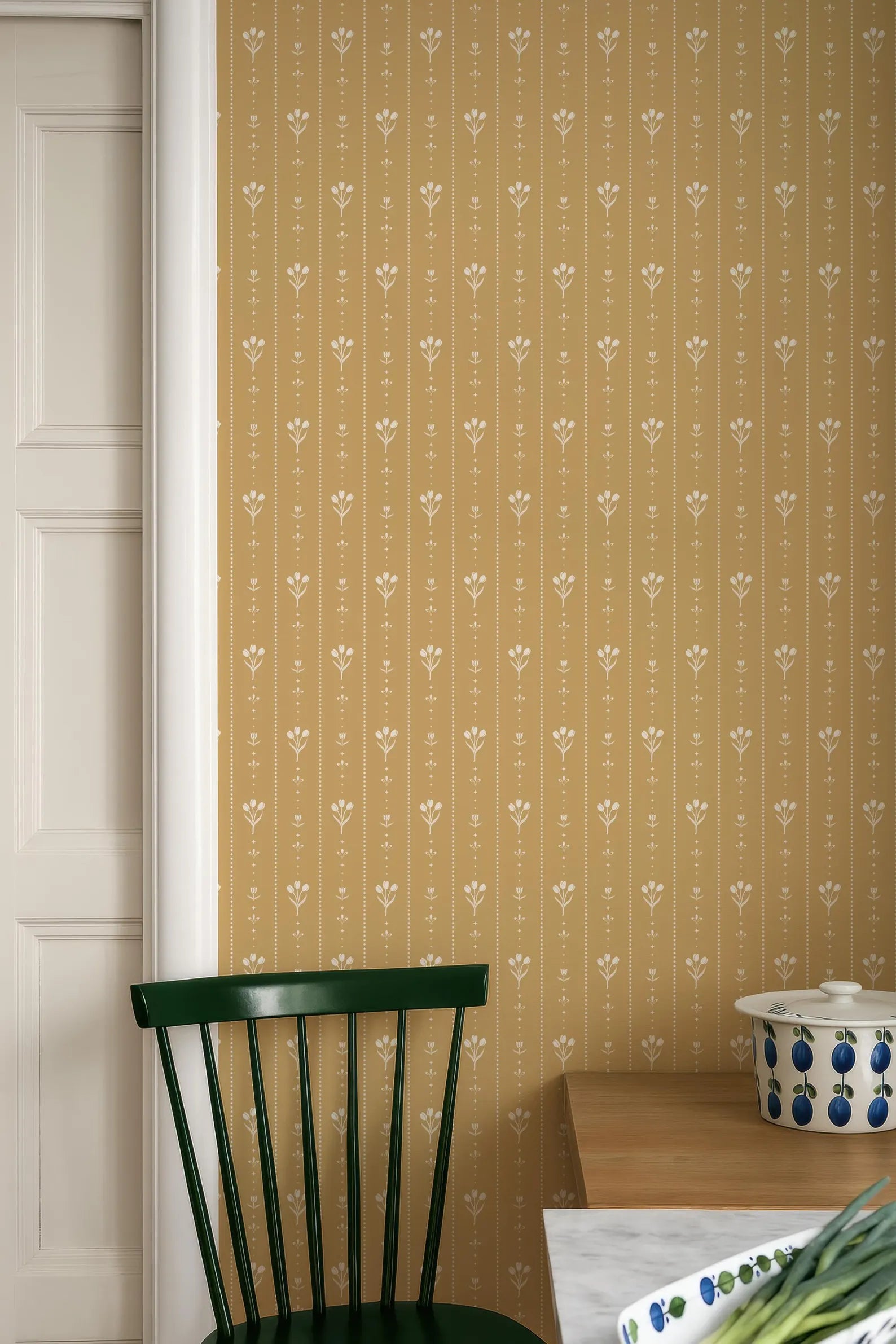 a kitchen setting with a green chair, a wooden table, and a patterned wall behind it.