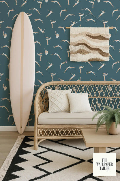 a living room with a wicker bench, a surfboard, and a woven wall hanging. The wall has a pattern of seagulls and waves, creating a beach-inspired atmosphere. The room also includes a rug and a potted plant, adding to the cozy and inviting ambiance.